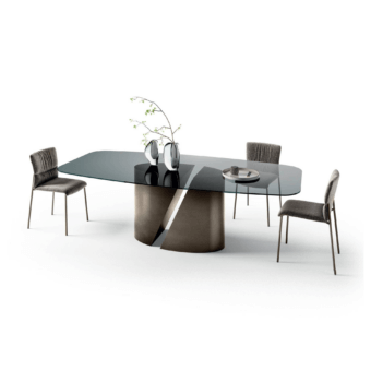 Glass dining table with dark gray sculptural base and silver accent, surrounded by four gray fabric chairs in a white studio setting.