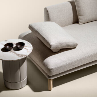 Beige modular sofa with square armrests and wooden legs, paired with a white marble side table featuring fluted base and brown ceramic bowls.