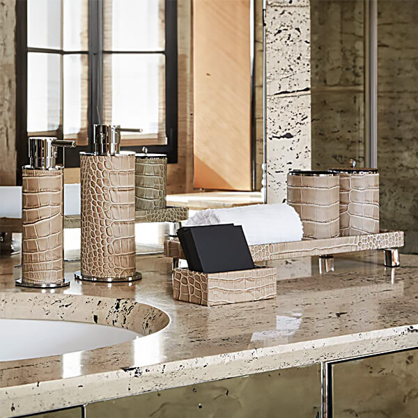 Beige & brown bathroom accessories on travertine marble: three textured cylindrical soap dispensers, towel tray, & square box.