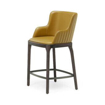 Luxury Magda Barré stool with smooth satin‑finish mustard‑yellow upholstery, dark wood frame, and matte‑grey metal footrest